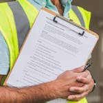 Person in Yellow Reflective Safety Vest Holding a Pen and Checklist of House Inspection