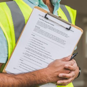 Person in Yellow Reflective Safety Vest Holding a Pen and Checklist of House Inspection